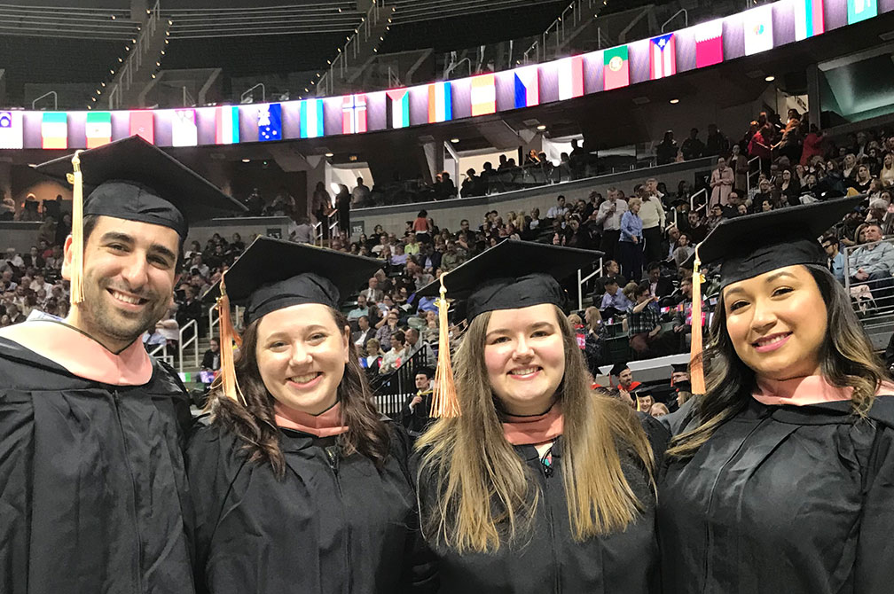 Four students smiling in graduation regalia