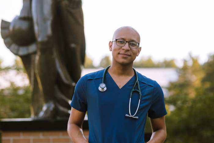Student wearing stethoscope and scrubs in front of Sparty statue